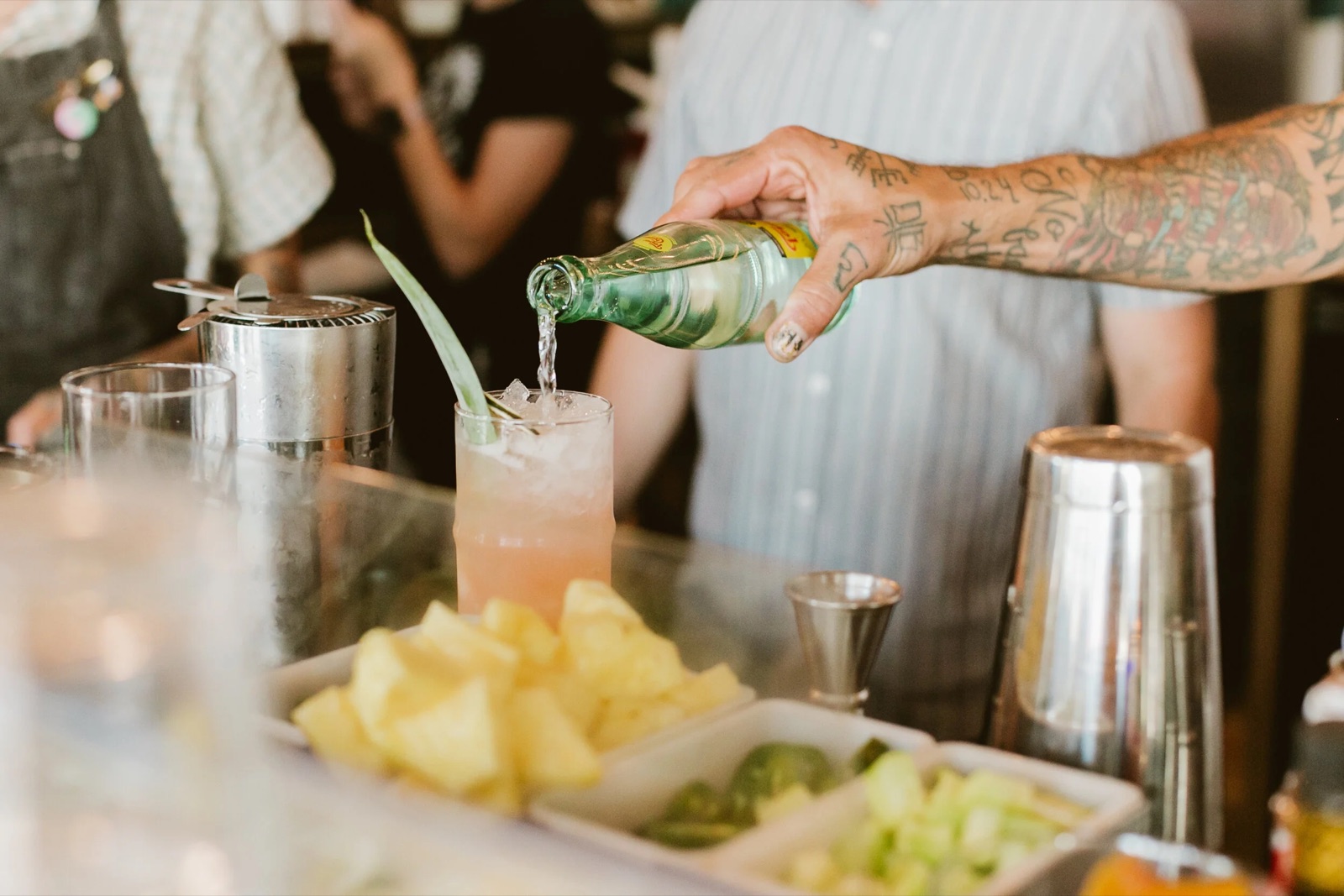 A bartender pouring a cocktail at the bar beside fresh pineapple